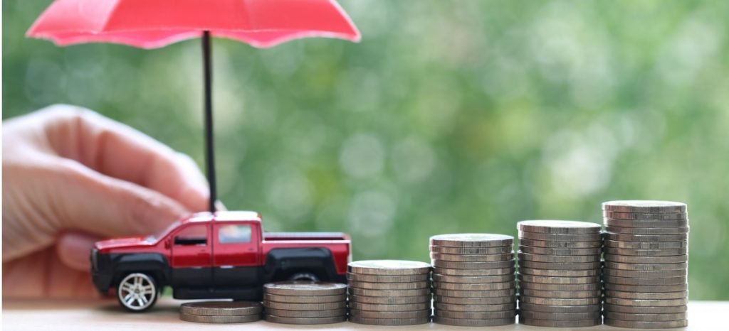 Miniature red car model on growing stack of coins money with hand holding the umbrella on green background